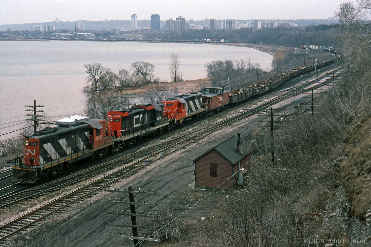 Powered by 3 GP9's, a train of mostly scrap metal loads in gondolas is climbing the grade from Hamilton Stuart St Yard, timetable eastbound on CN's Oakville Sub (compass north). It looks like traffic for Lake Erie Steel at Nanticoke, in which case it will switch onto to the "Cowpath" just ahead to head west on the Dundas Sub. 
Note there are cabooses at both ends of the train, and middle loco CN 4514 has fabricated winterization covers, suitable for snowplow service.